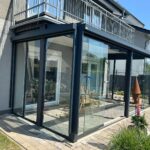 Kompakter Kaltwintergarten in Anthrazit mit geöffneter Ganzglasschiebeanlage und Blick in den Garten